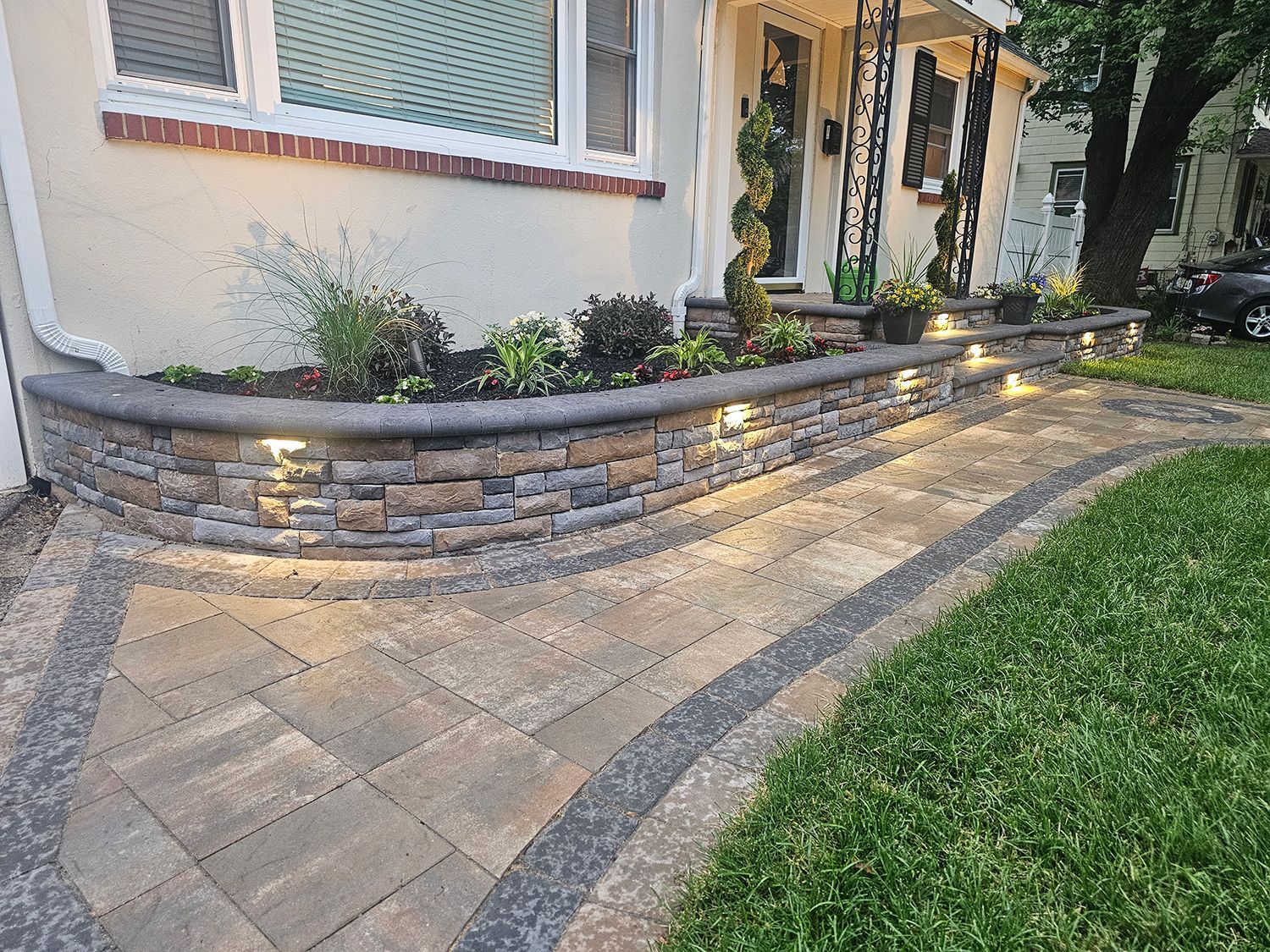 A stone walkway leading to the front of a house with lights on it.