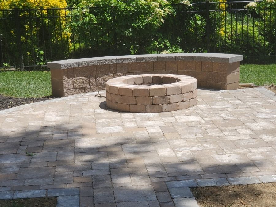 A brick patio with a fire pit and a bench