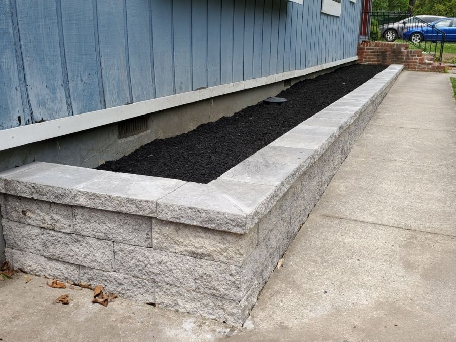 A concrete wall with a planter in front of a blue house.