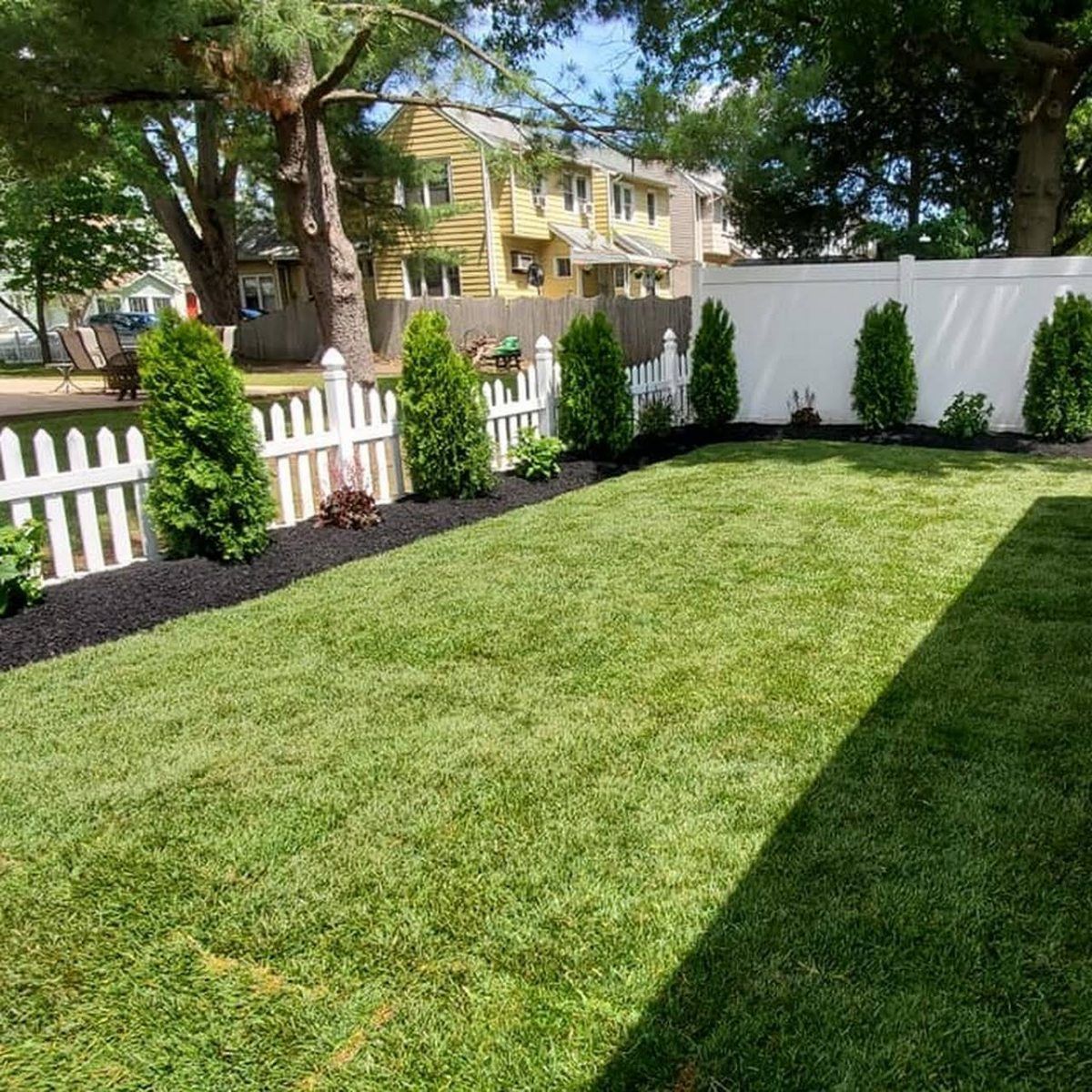 A backyard with a white picket fence and a lush green lawn.