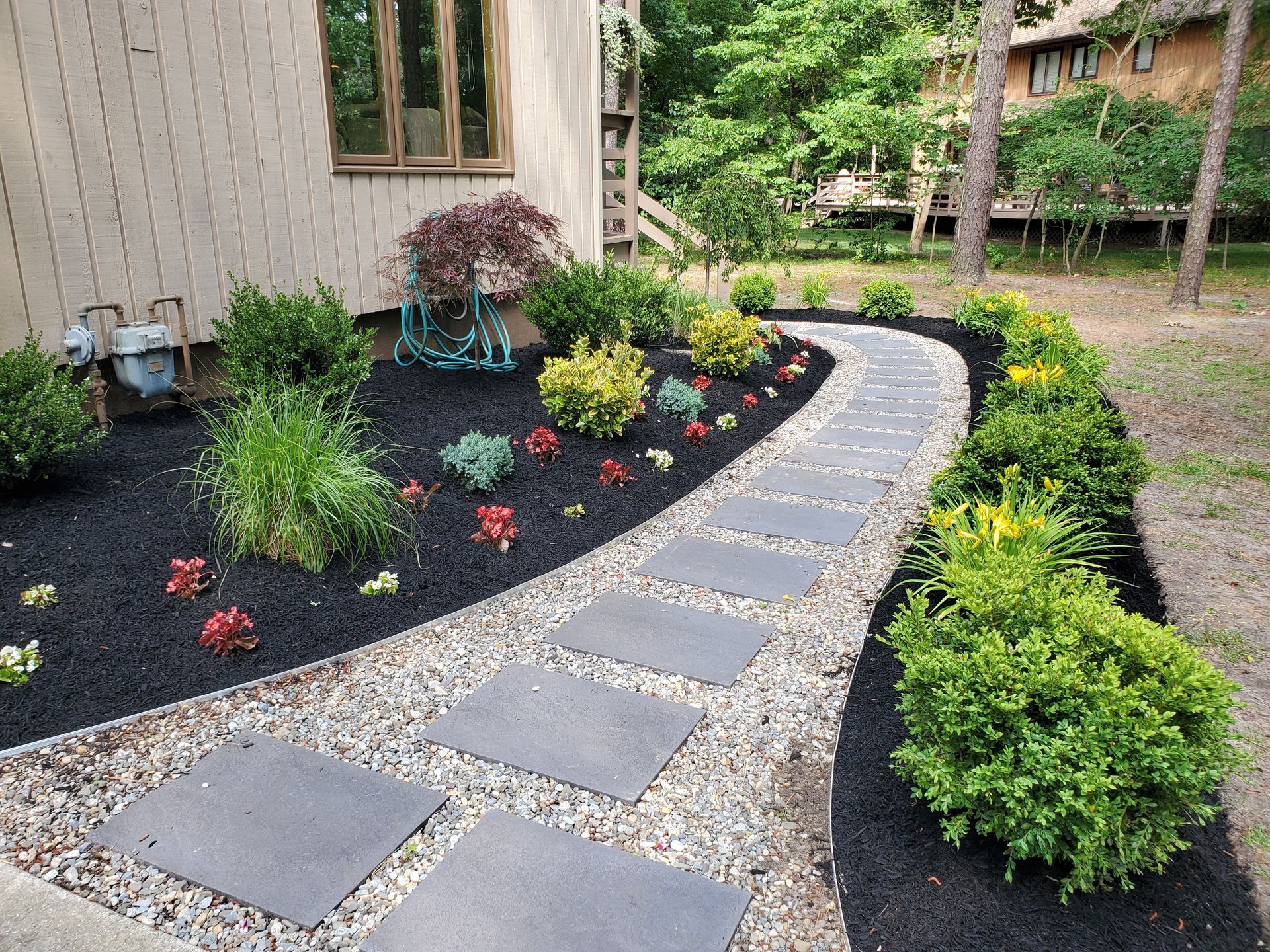A stone walkway leading to a house surrounded by plants and bushes.