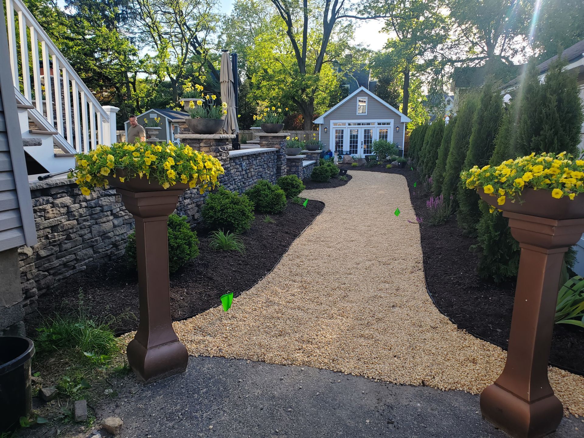 A walkway leading to a house with two planters filled with yellow flowers.