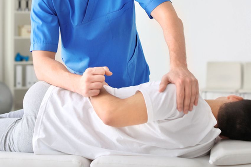 A man is laying on a bed getting a massage from a doctor.