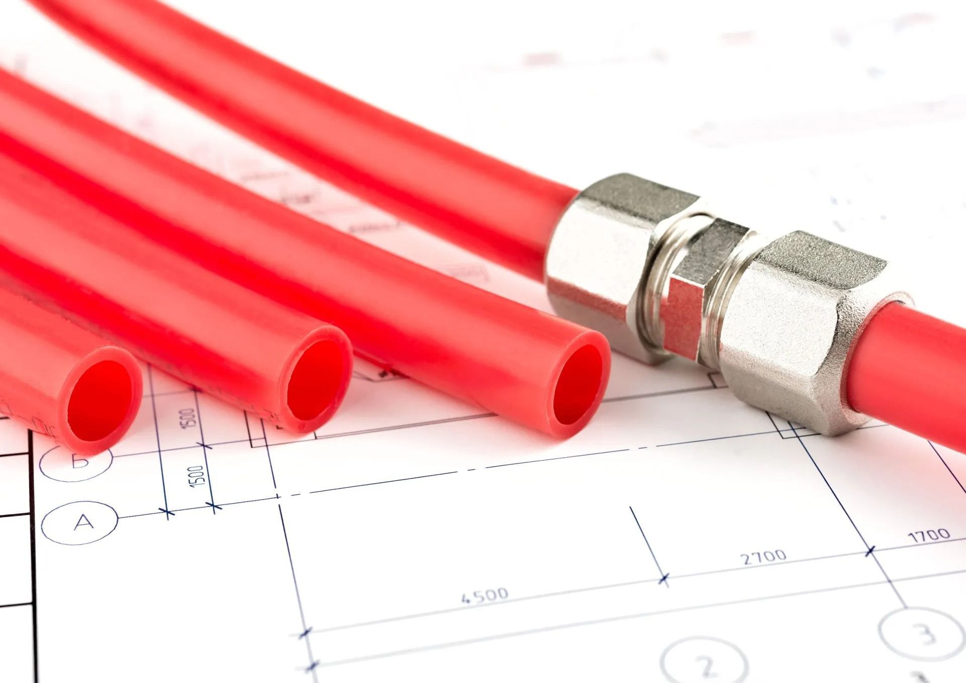 Red PEX plumbing pipes and a metal connector sit on an architectural blueprint.