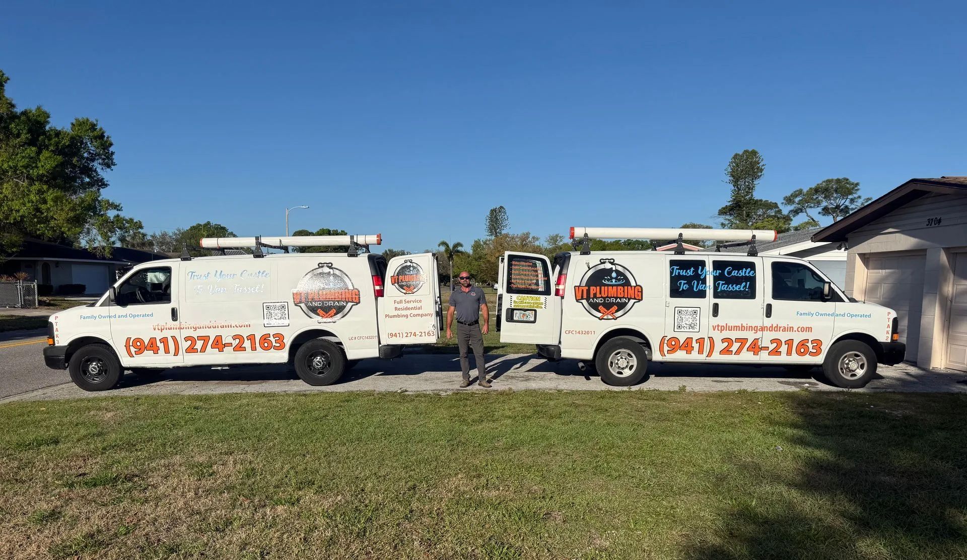Two white service vans with orange logos parked side by side on a grassy roadside under a blue sky.