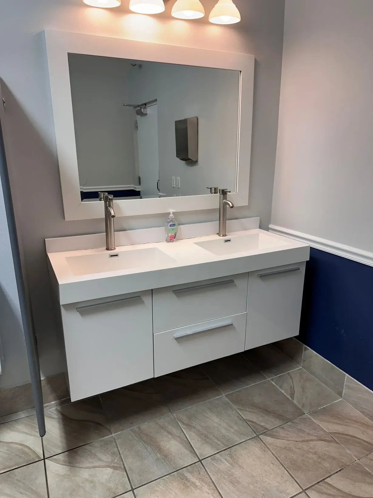 Modern bathroom vanity with double sinks, large mirror, and wall lights over gray tile floor.