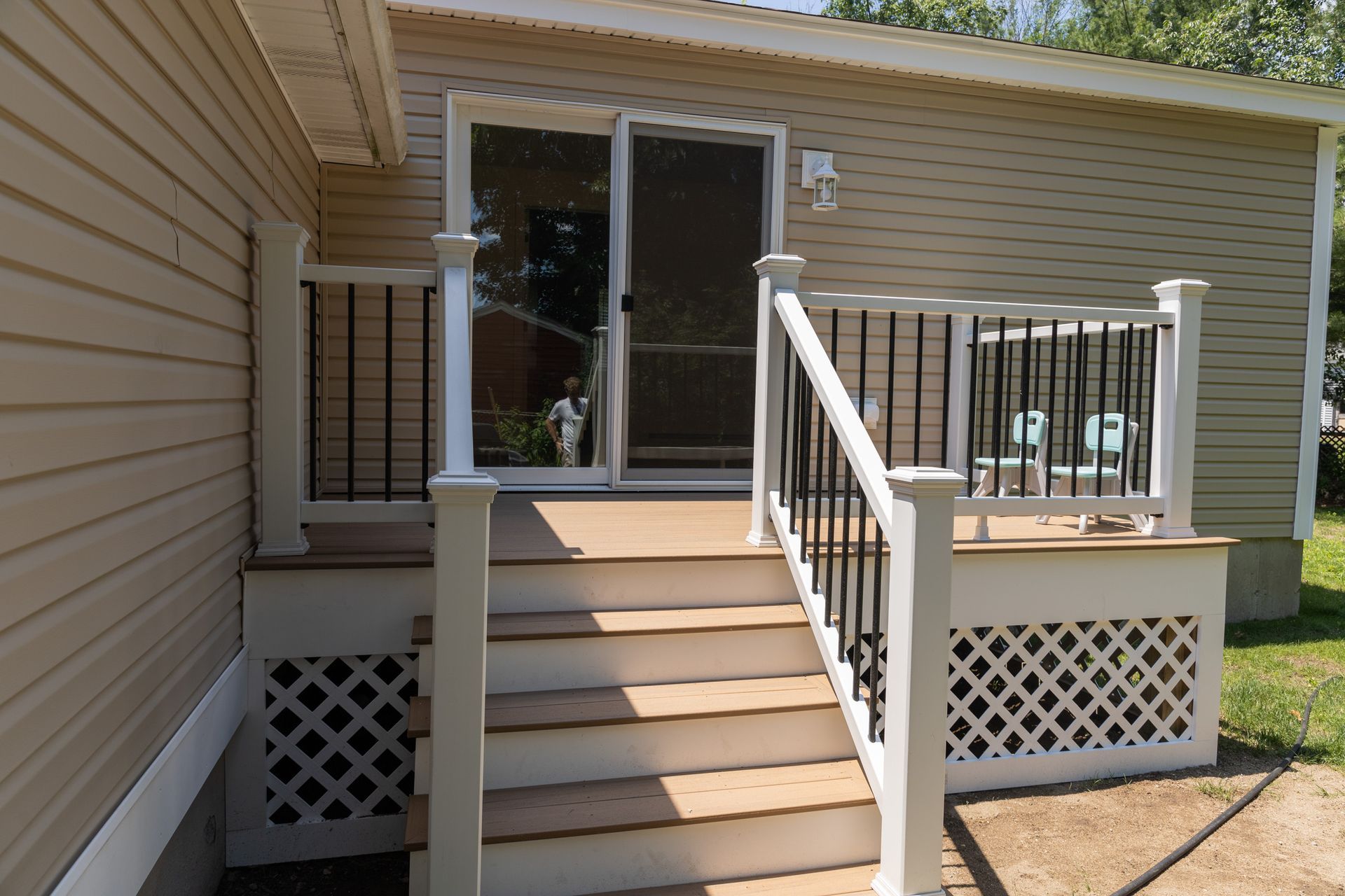 A beige house with a tan composite deck and matching stairs, white railings, black balusters, and white lattice skirting.