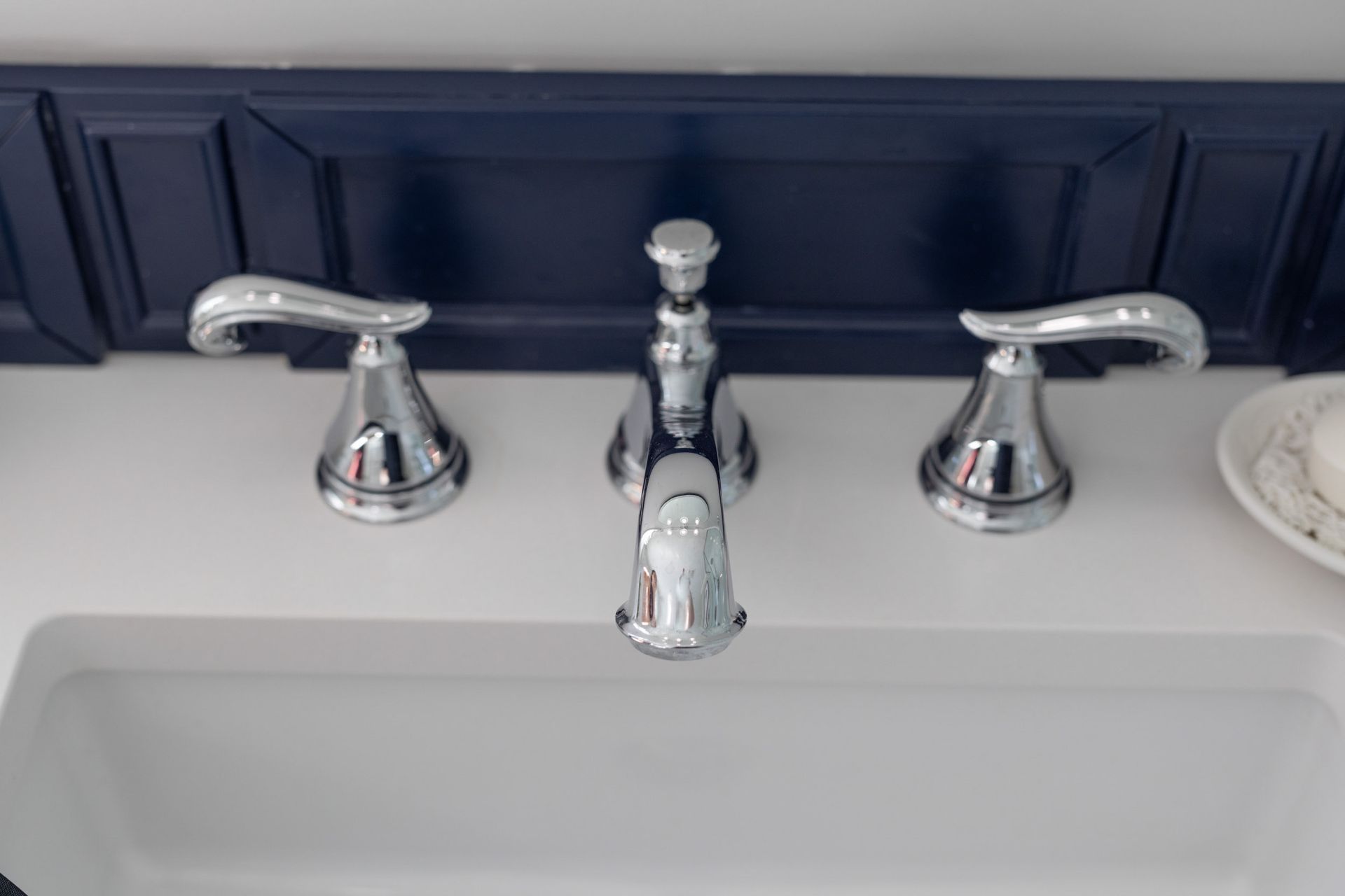 A chrome bathroom faucet set with two handles and a central spout, set against a dark blue backsplash and white counter.