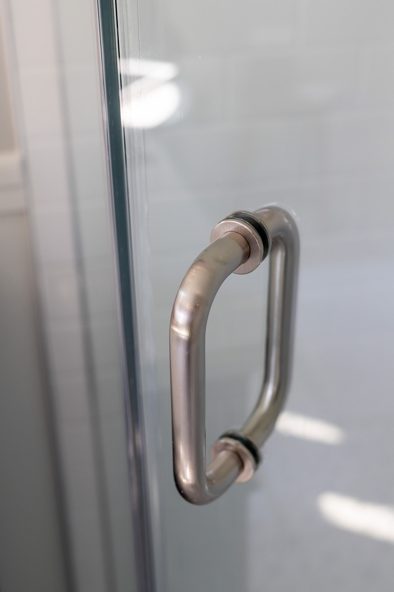 A brushed nickel metal handle attached to a glass shower door with visible rubber gaskets.