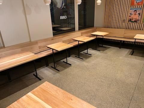 A clean interior space featuring light wooden tables and built-in bench seating along a slatted wall.