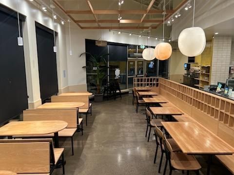 An empty cafe interior with light wood booths, tables, and minimalist globe pendant lights over a concrete floor.