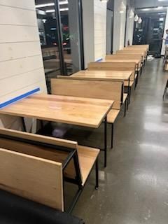 A row of wooden tables with attached bench seating lining a wall in a modern, brightly lit indoor space.
