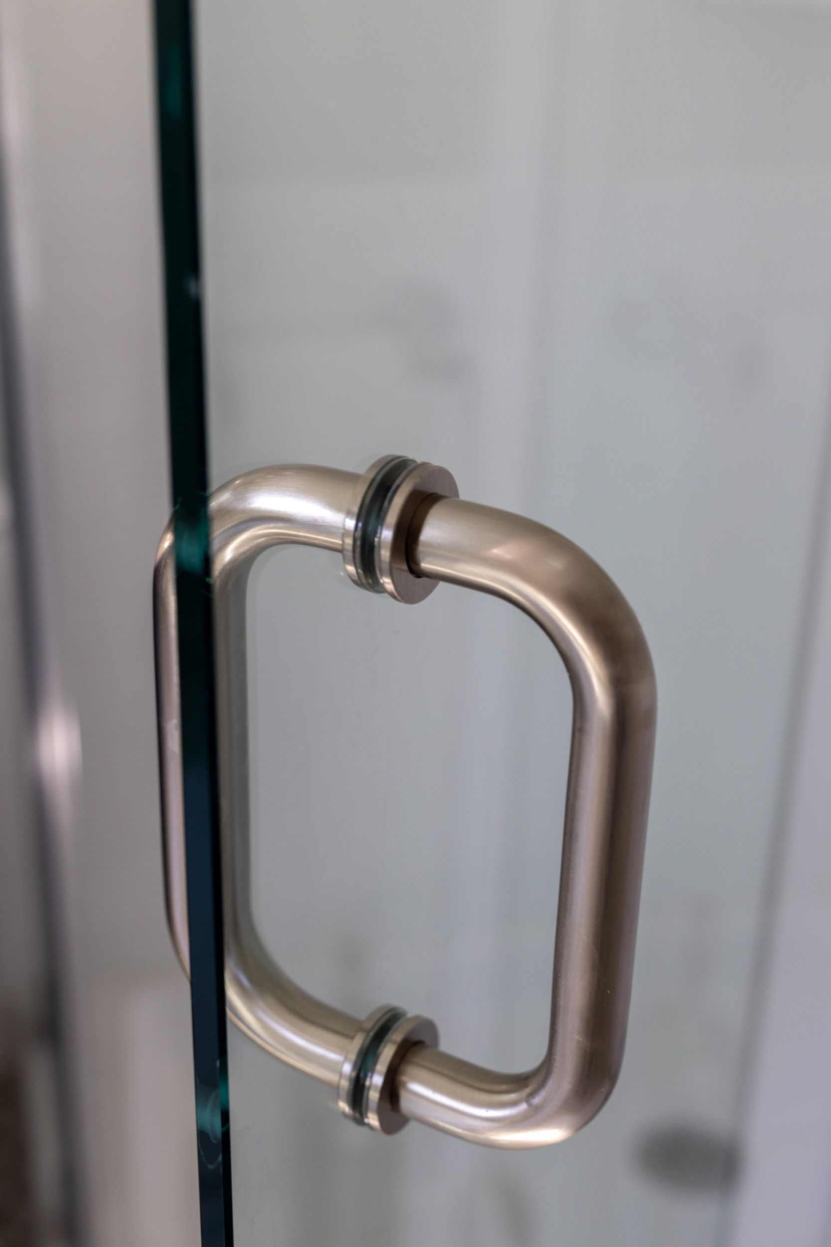 Close-up of a brushed metal D-shaped handle attached to a glass shower door.