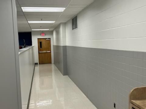 A hallway with white upper walls, gray lower walls, a glossy floor, and a wooden door at the far end.