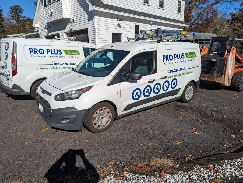 Two white Pro Plus service vans parked outside a white building with a piece of construction equipment on the right.