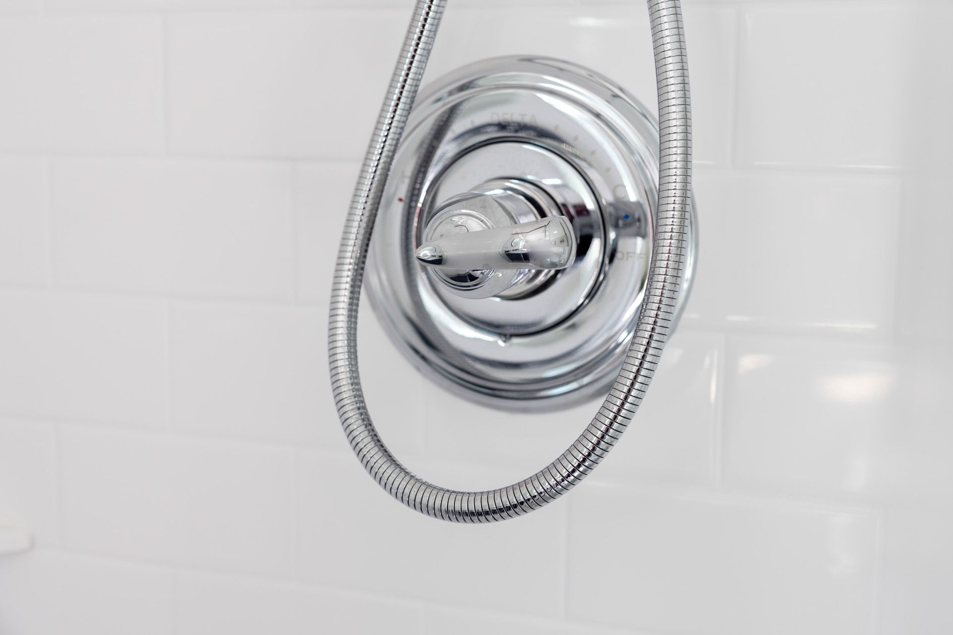 A chrome shower faucet handle and circular trim plate mounted on a wall with white rectangular tiles.