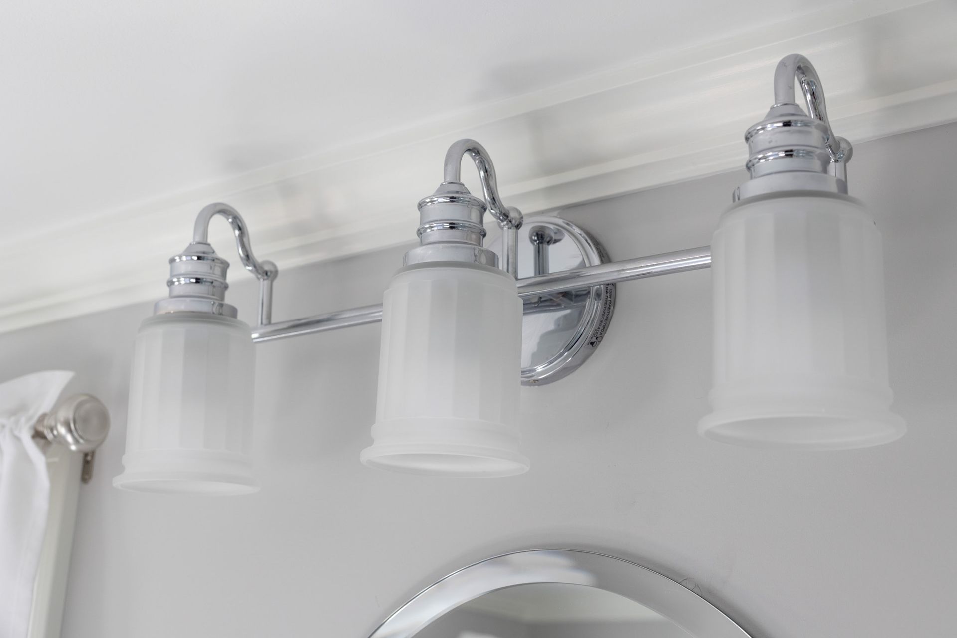 A three-light vanity fixture with chrome hardware and frosted glass shades mounted on a light gray wall.