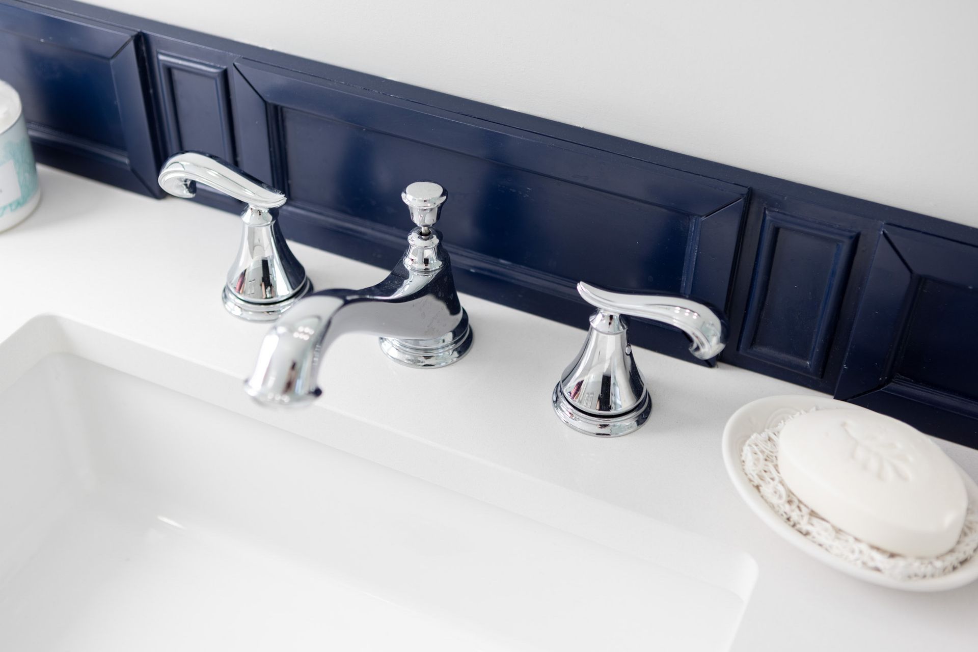 Chrome bathroom faucet on a white vanity counter against a dark navy blue paneled wall, with a bar of soap nearby.