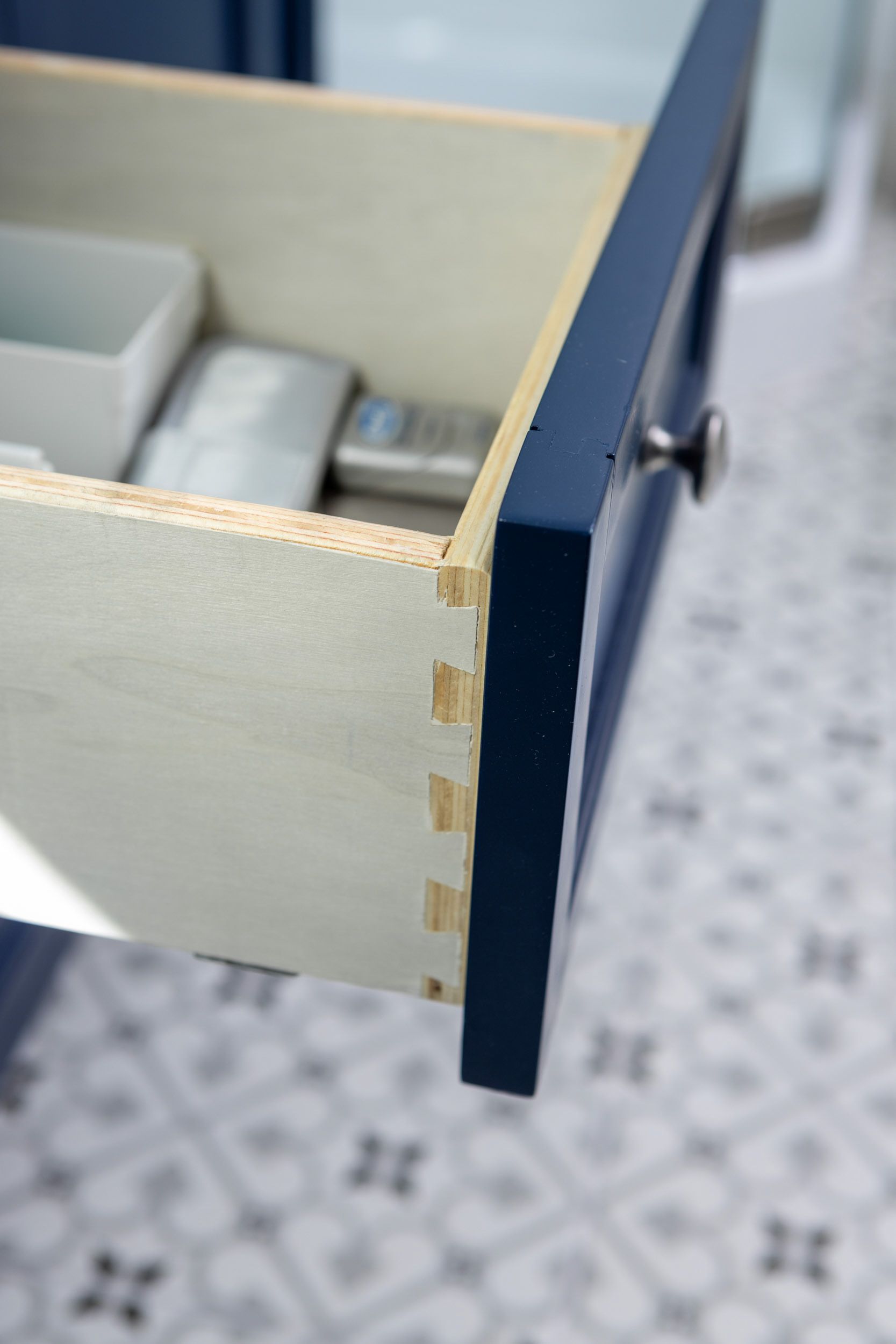 A close-up view of a dark blue drawer front joined to light wood side panels with exposed finger joint construction.