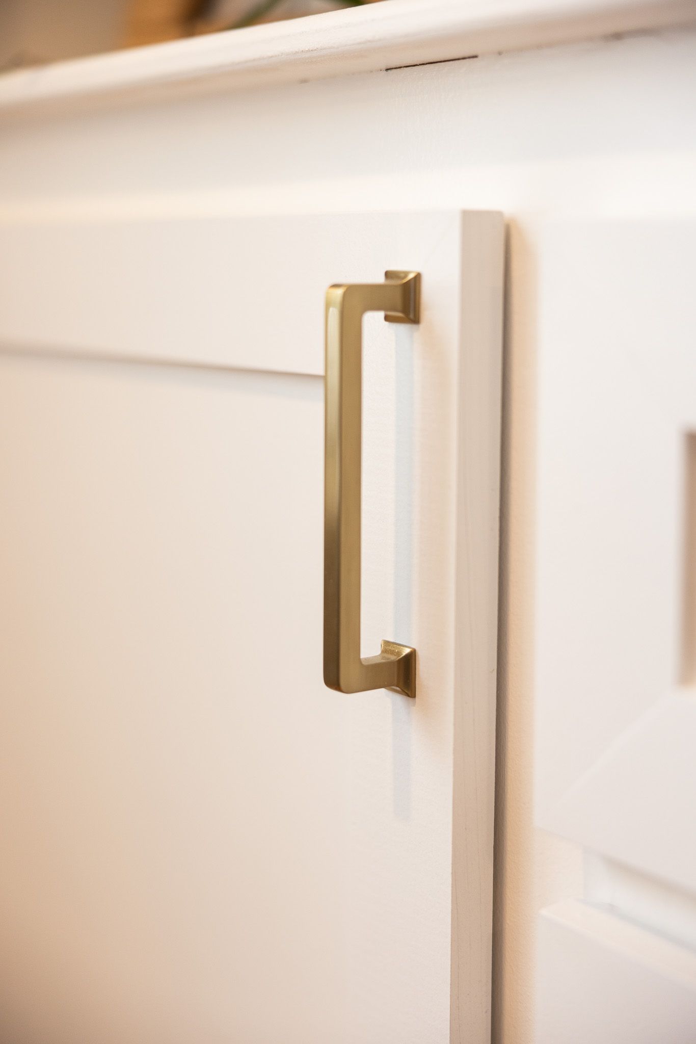 Close-up of a matte gold modern cabinet handle mounted on a clean white shaker-style cabinet door.