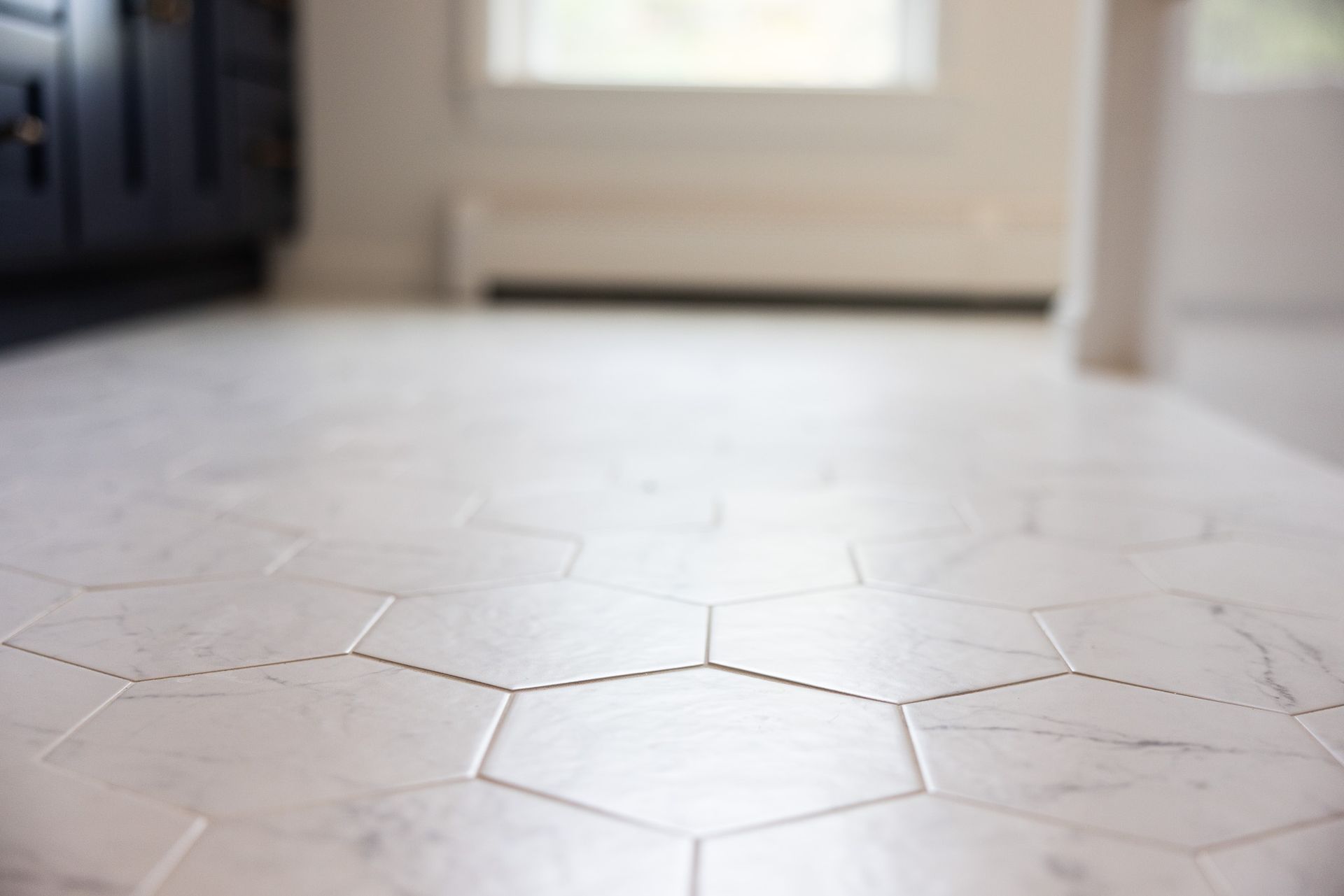 White hexagonal floor tiles with subtle grey marble veining in a bright indoor room.