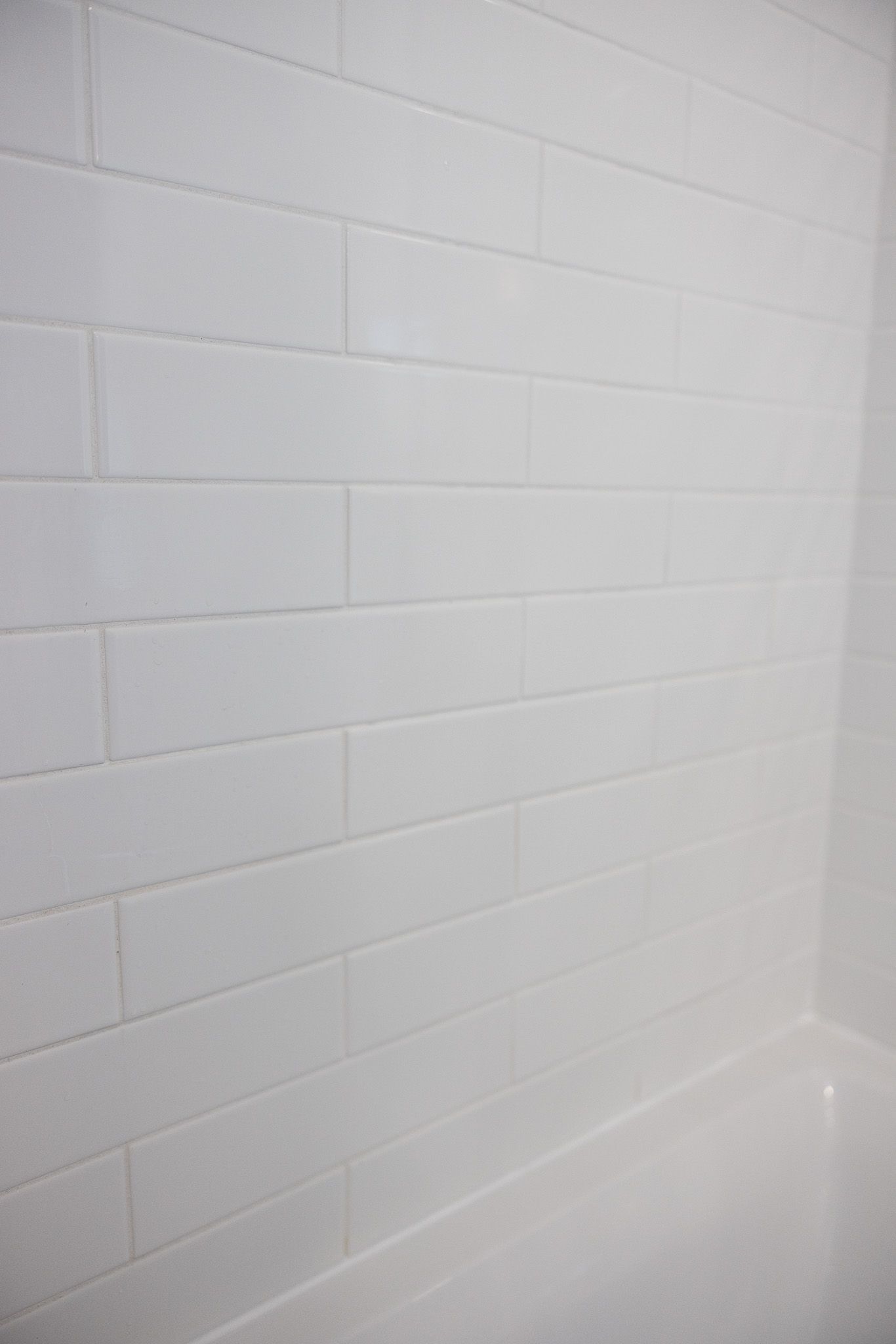 A close-up view of white, rectangular bathroom wall tiles installed in a running bond pattern above a white tub.