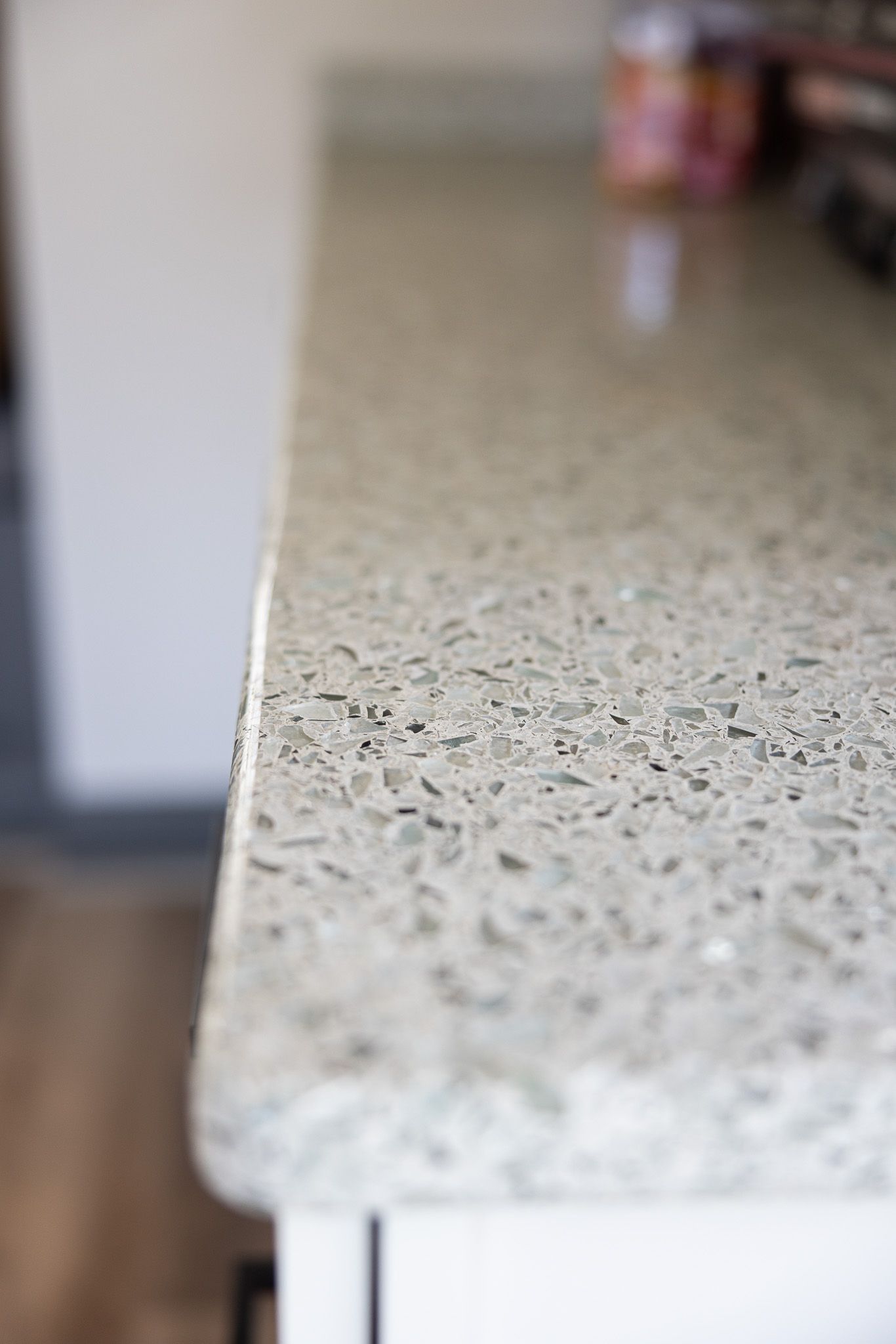 A close-up of a speckled, light gray concrete countertop with a rounded edge sitting on white cabinetry.
