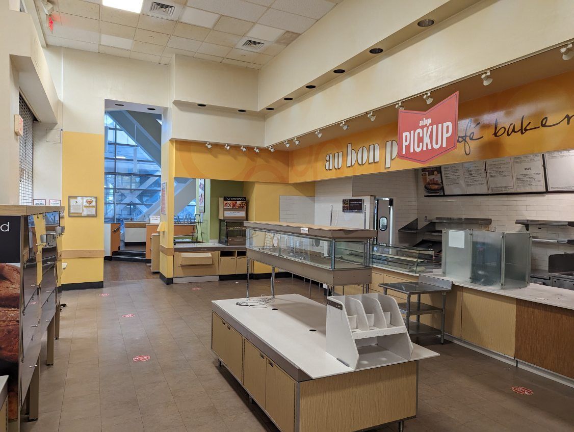 A view of an empty Panera Bread counter with a pickup sign, food display cases, and warm-toned yellow walls.