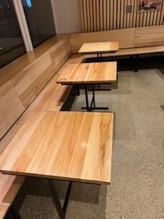 Light-wood cafe tables and attached bench seating in a restaurant with light-colored flooring and a slatted wood wall.