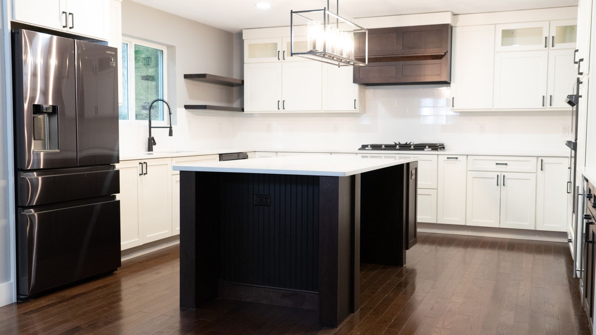 A modern kitchen featuring white cabinets, a dark wood central island, stainless steel refrigerator, and wood flooring.