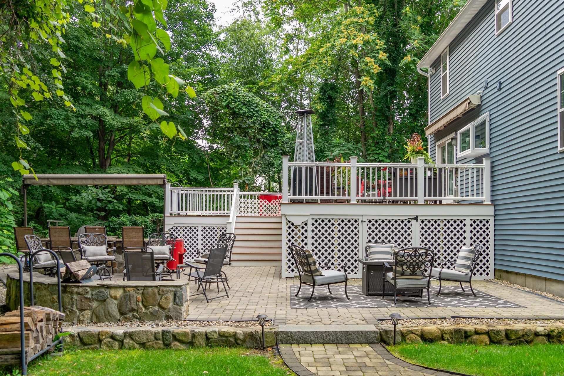 A back patio featuring a stone seating wall, dining furniture, a fire pit, and stairs leading up to a raised deck.