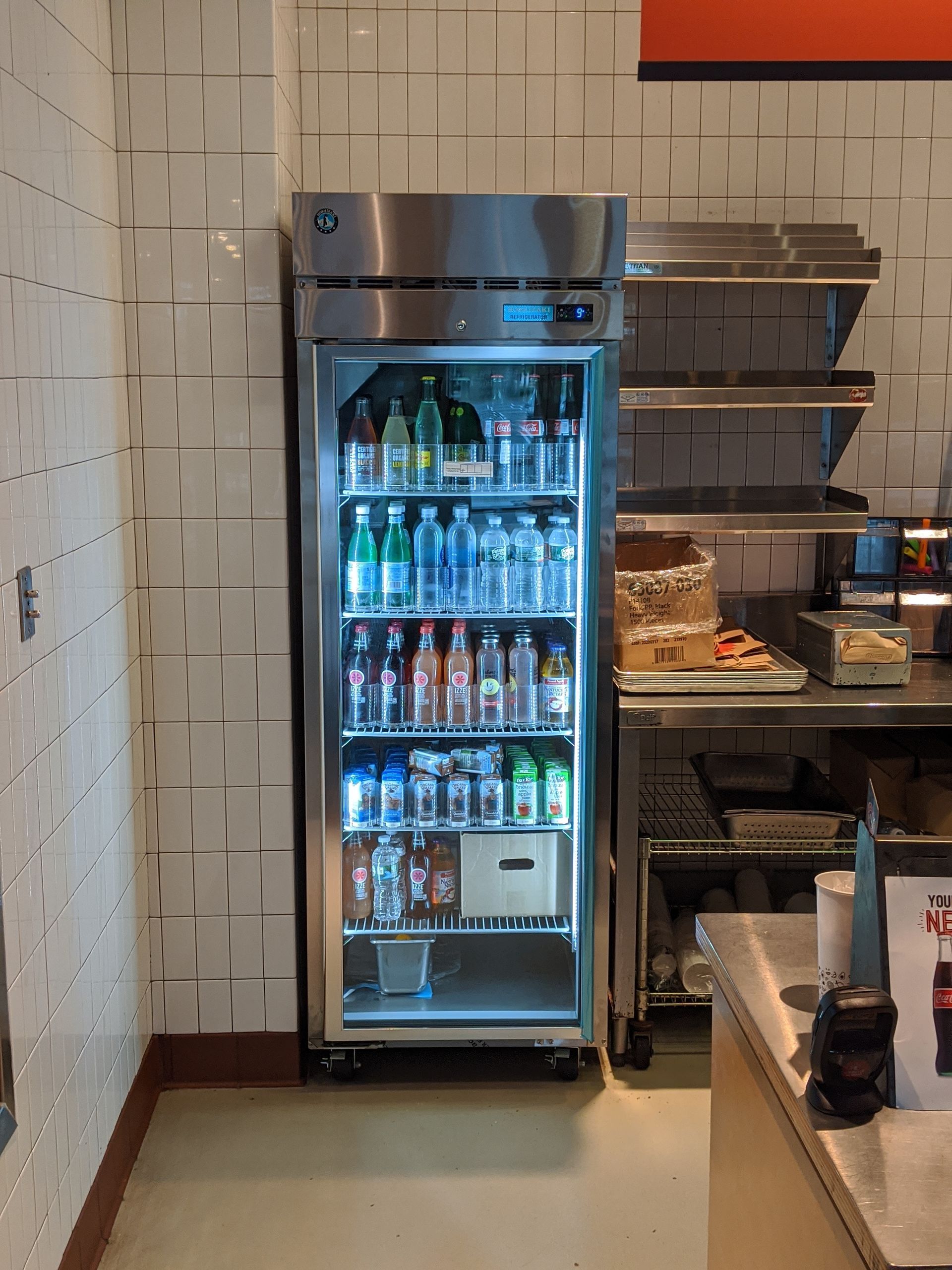 A stainless steel reach-in refrigerator with glass doors displaying assorted bottled and canned beverages.