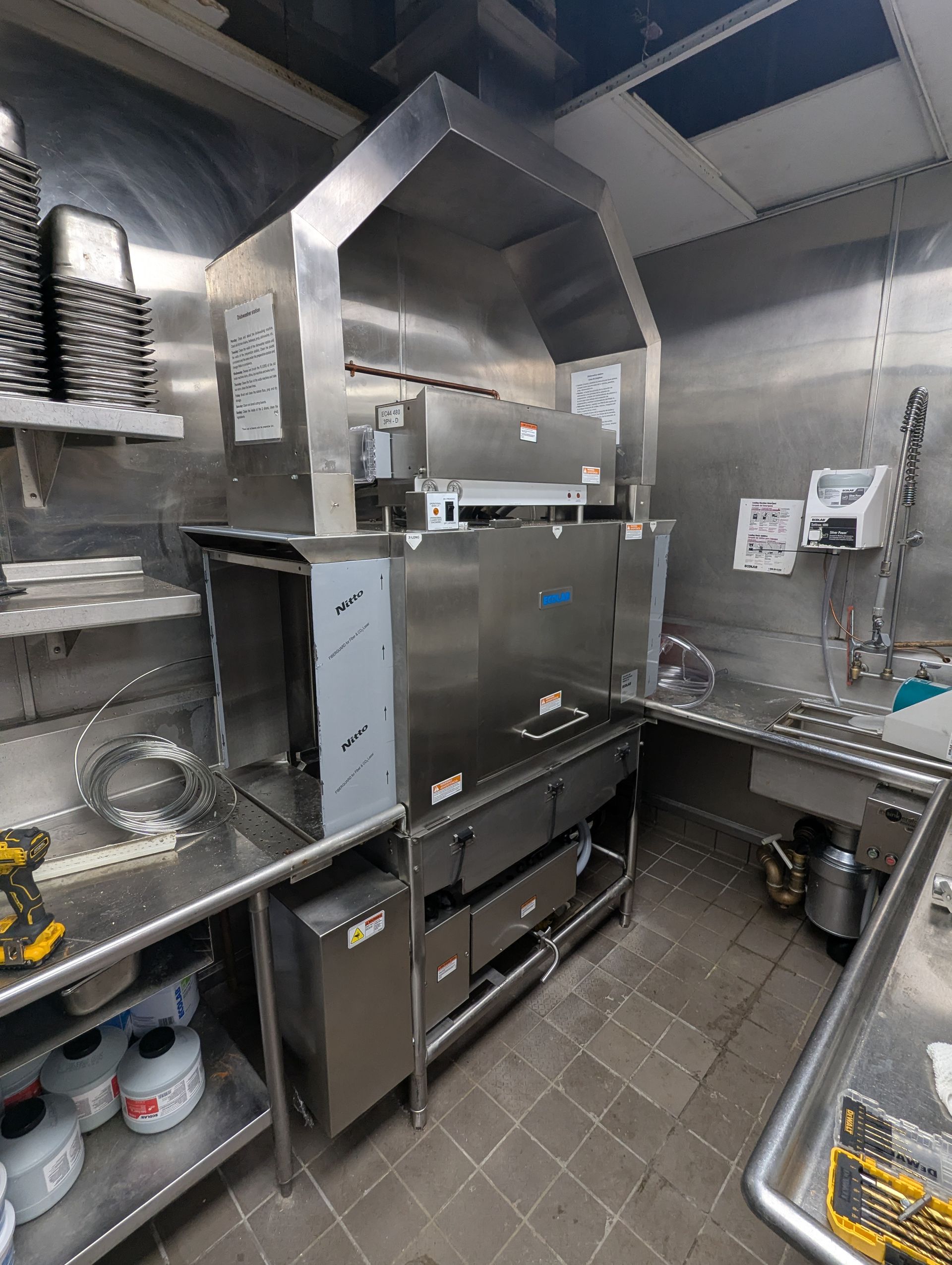 Commercial stainless steel dishwasher station with an overhead ventilation hood in a professional kitchen.