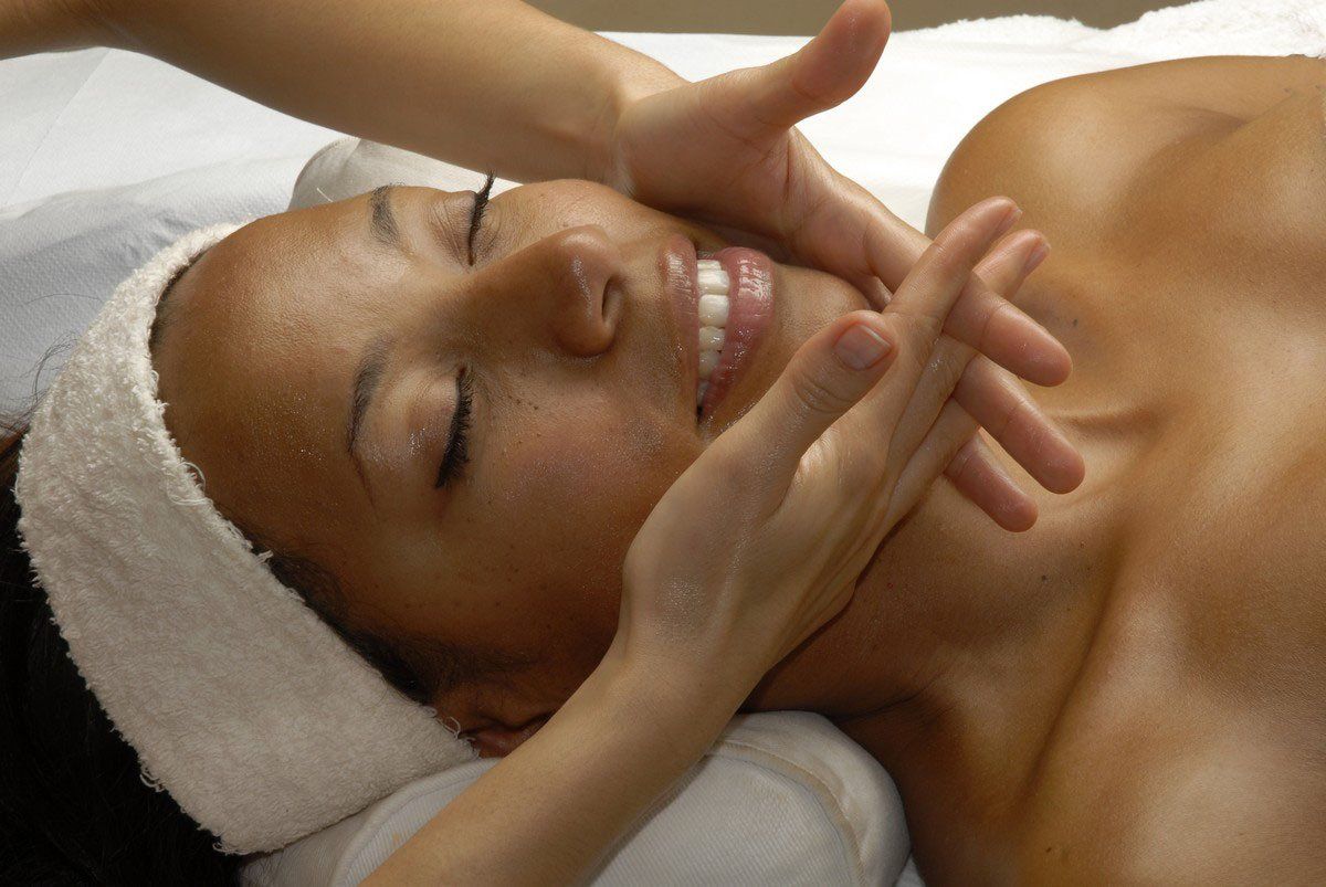 Woman receiving facial massage, face close up. Hands on cheeks, lying on towel, eyes closed, smiling.