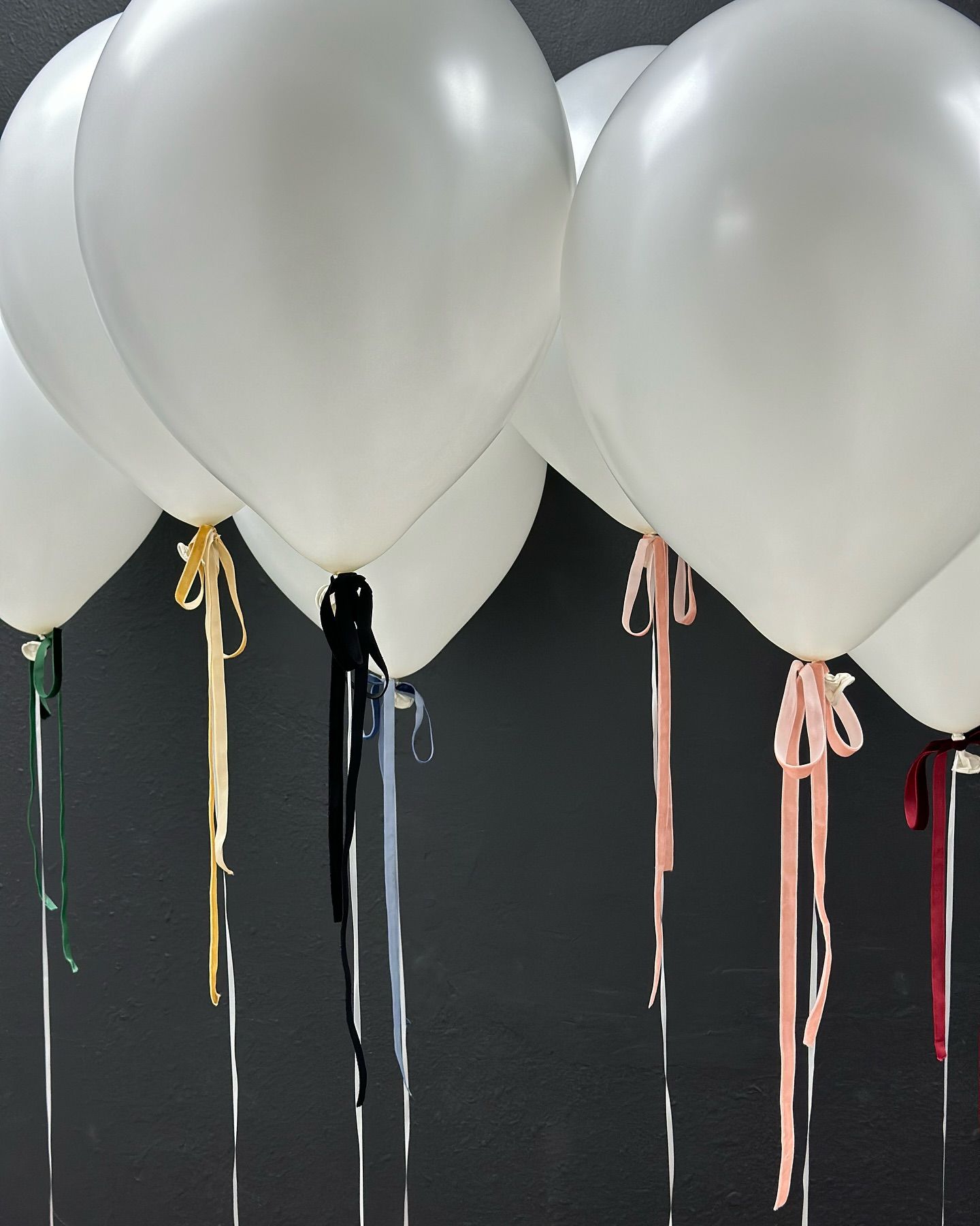 A bunch of white balloons with ribbons attached to them