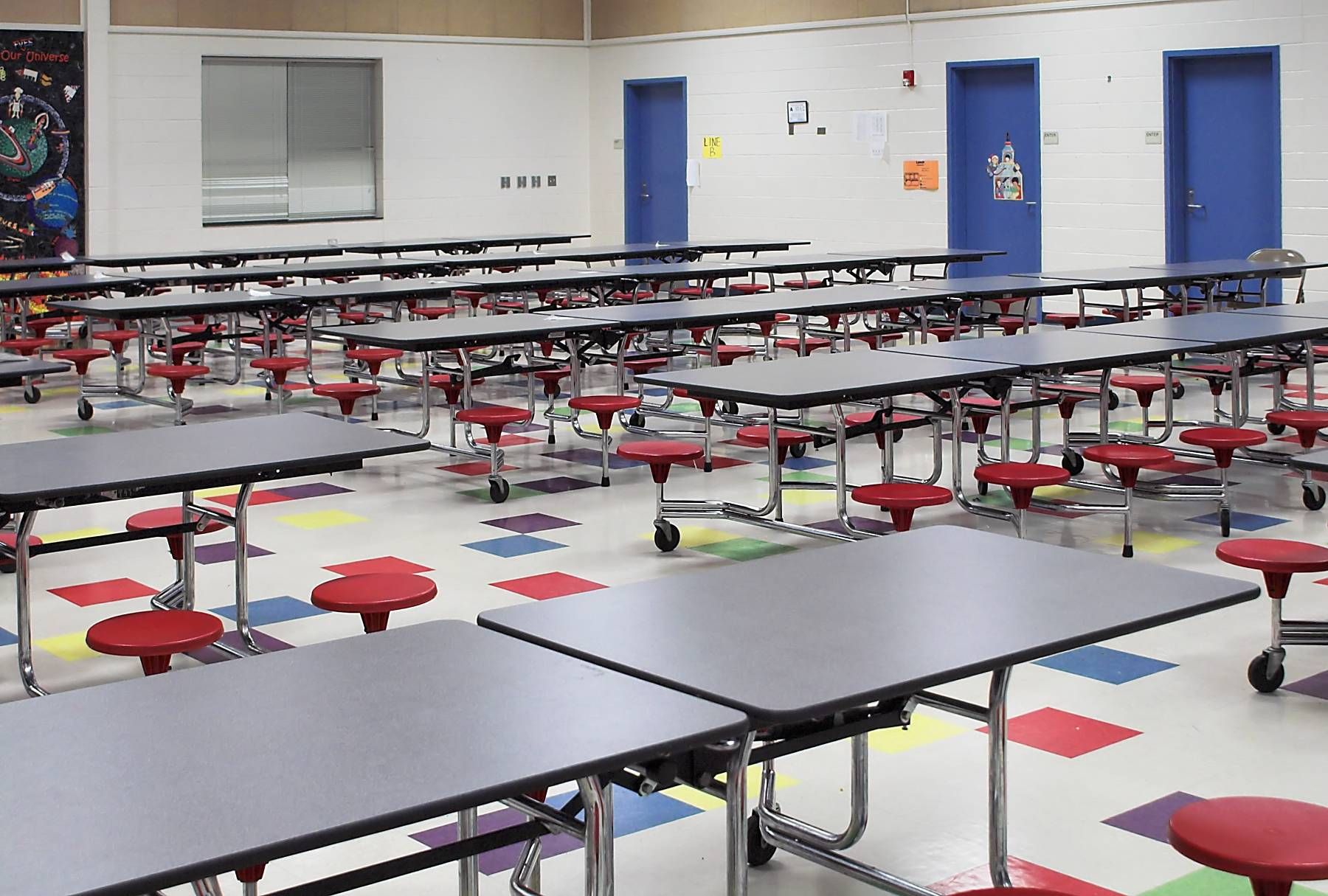 An empty school cafeteria with tables and stools