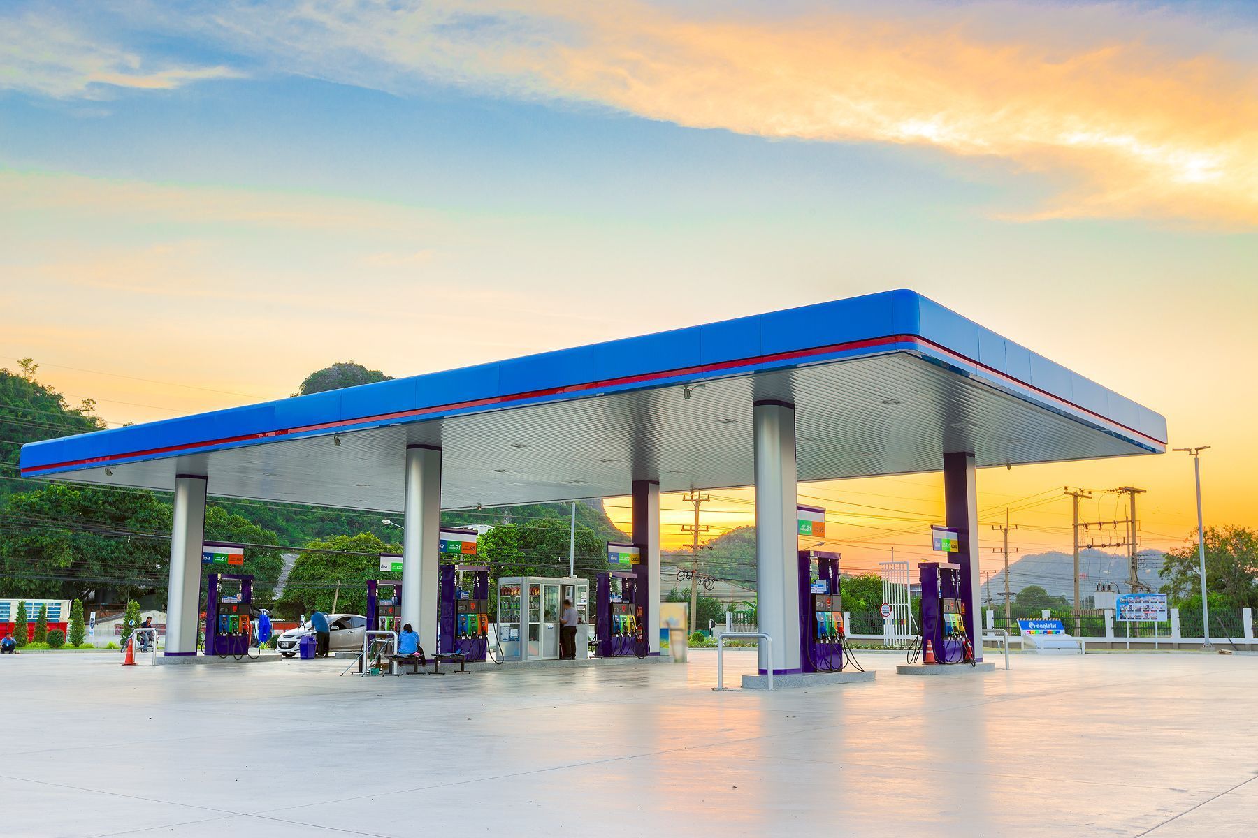 A gas station with a blue roof and a sunset in the background.