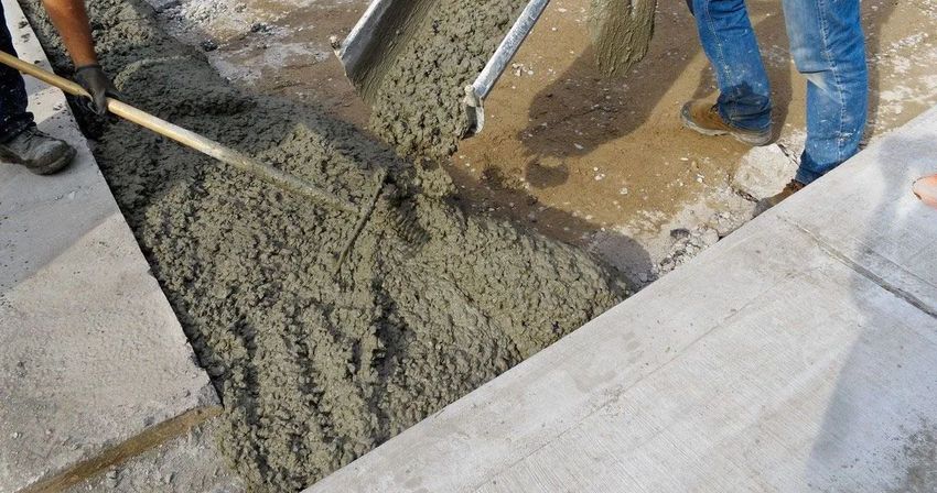 Workers pouring concrete, leveling with rake, on a sidewalk, gray and wet.