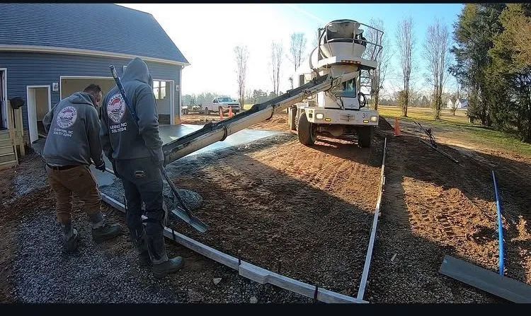 Two workers pouring concrete driveway from a cement truck at a house under construction.