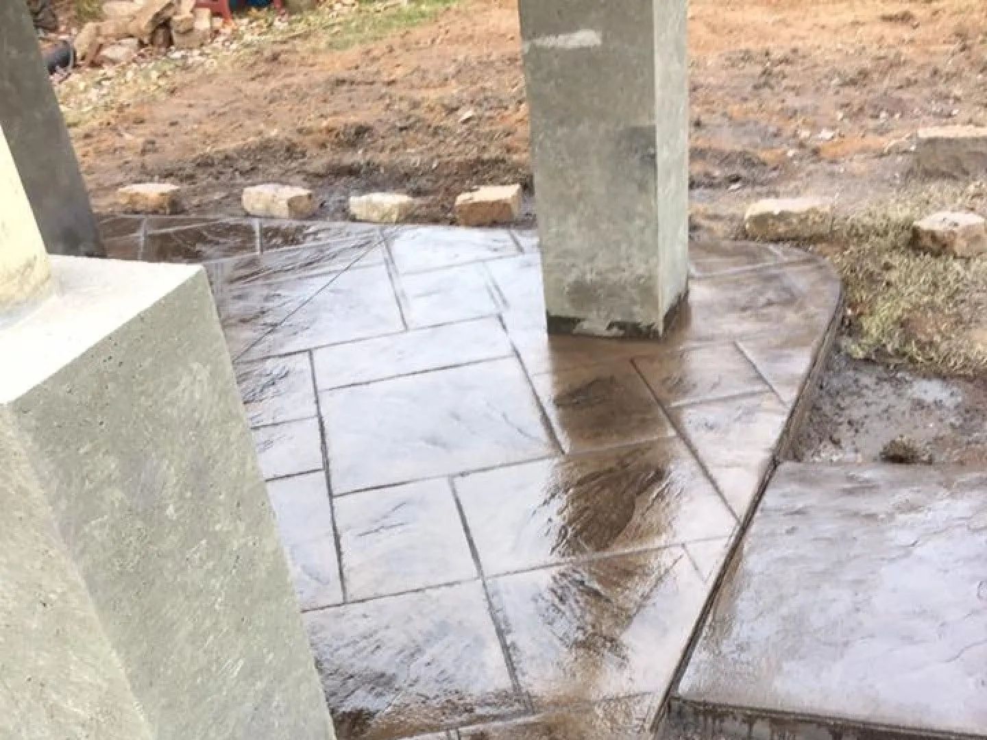 Wet, dark paving stones laid around concrete pillars in a construction site.