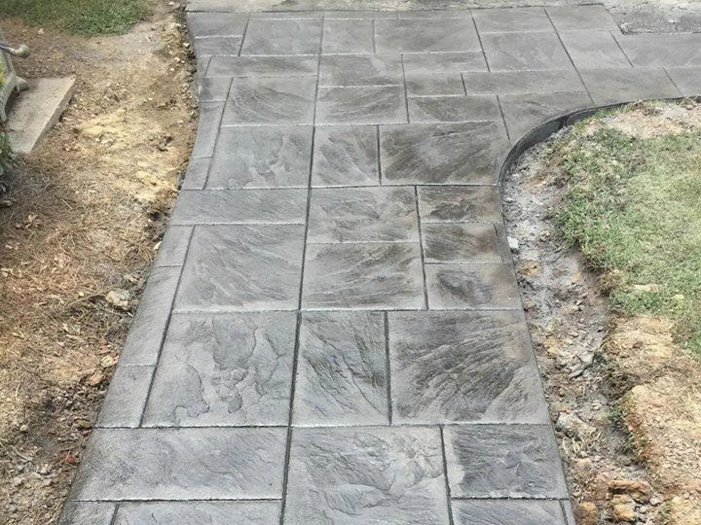 Gray stamped concrete walkway with a curved edge and a textured stone pattern.