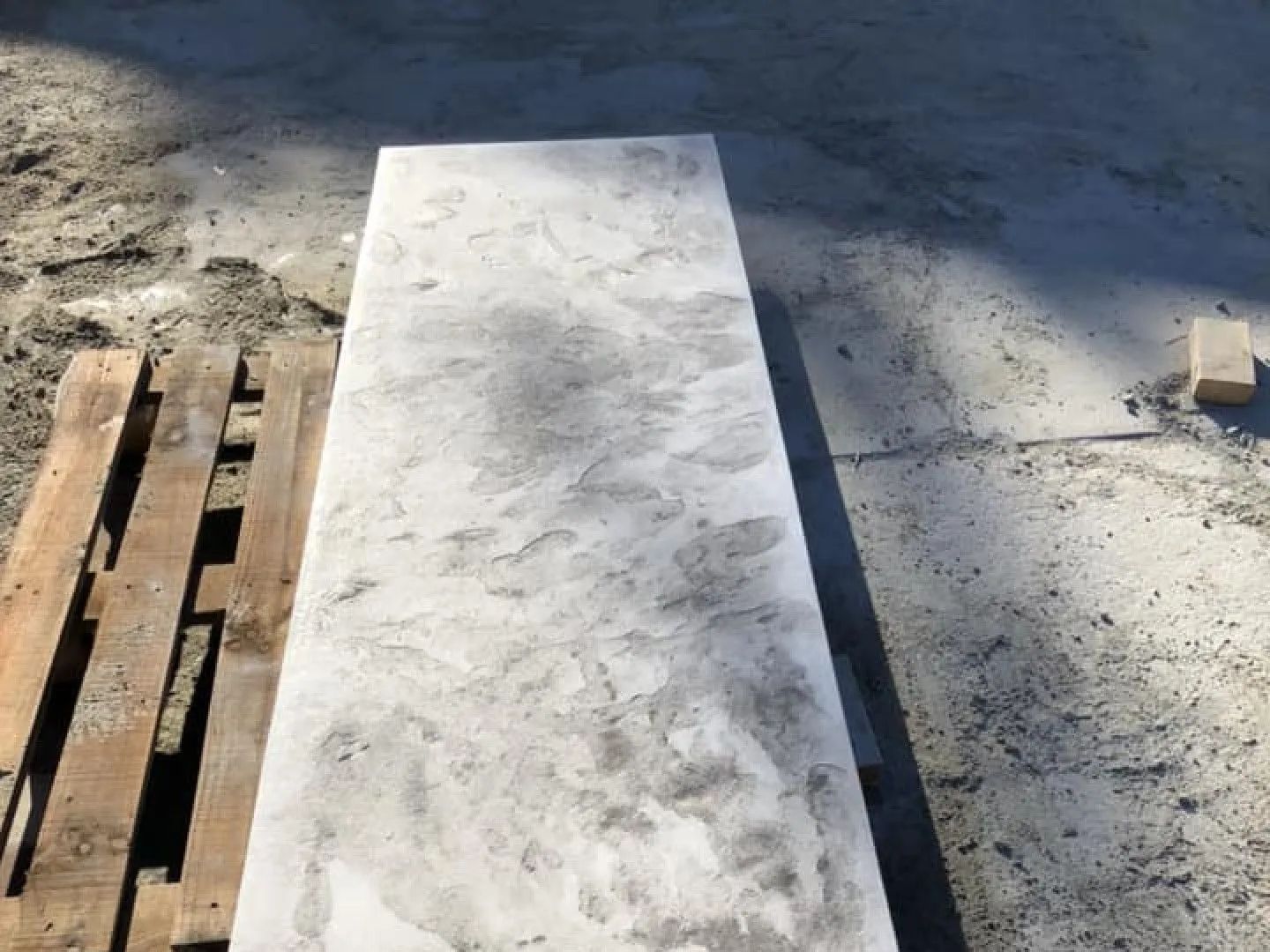 Rectangular concrete slab with mottled gray and white pattern on a construction site next to a wooden pallet.
