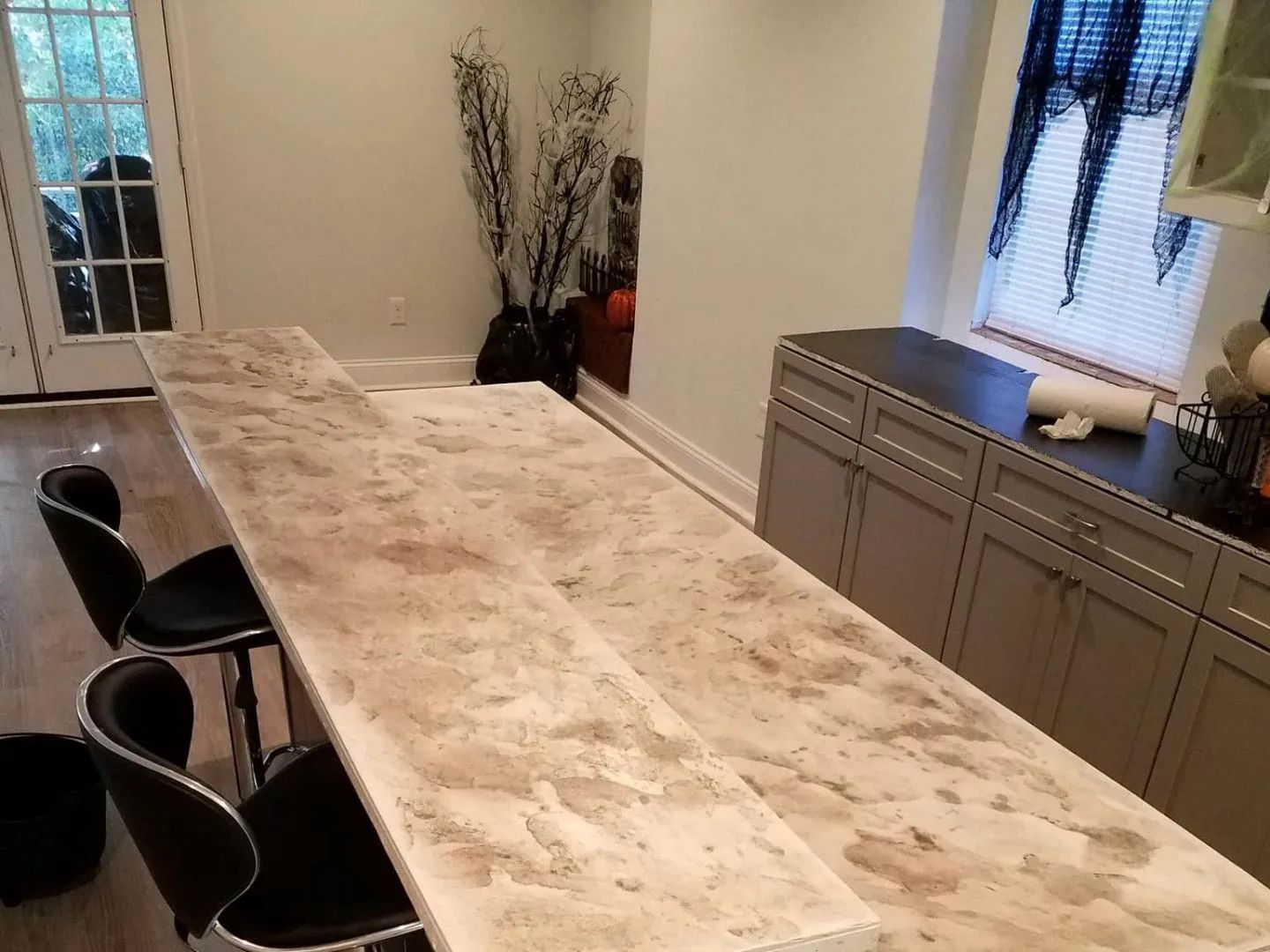 Kitchen with a long, light-colored countertop, bar stools, and cabinets.