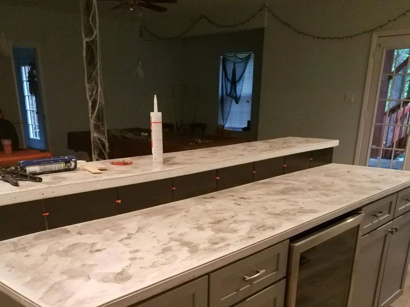 Bar with gray cabinets, concrete countertops, and a dark brown panel with a caulk gun.