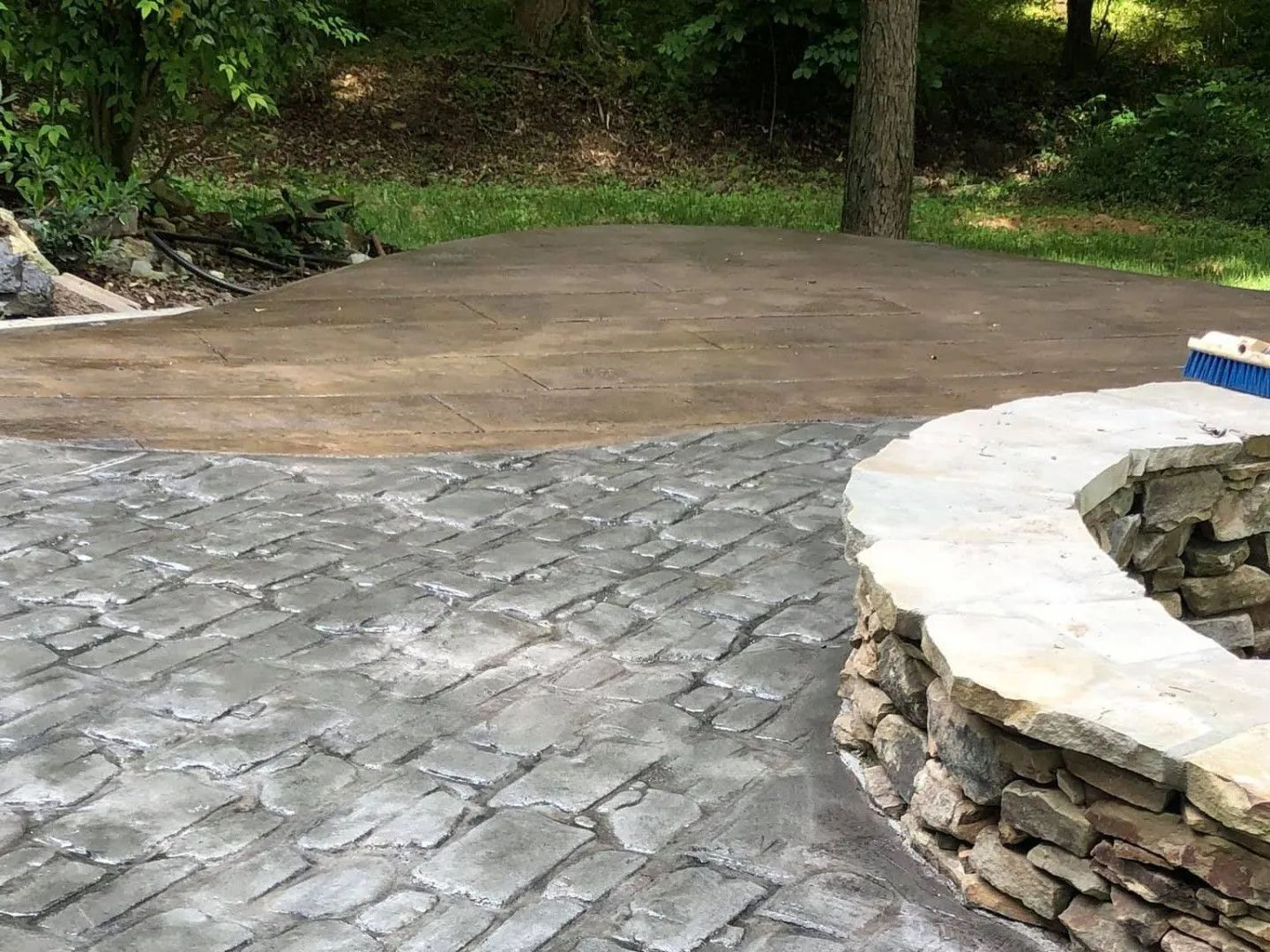 Stone patio with a fire pit transitions to a graded, dirt area near trees.