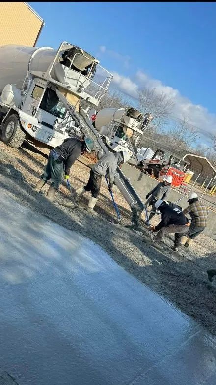 Workers pouring concrete from a truck onto a surface on a sunny day.