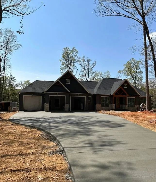 A house with a black roof, two-car garage, and concrete driveway on a sunny day.