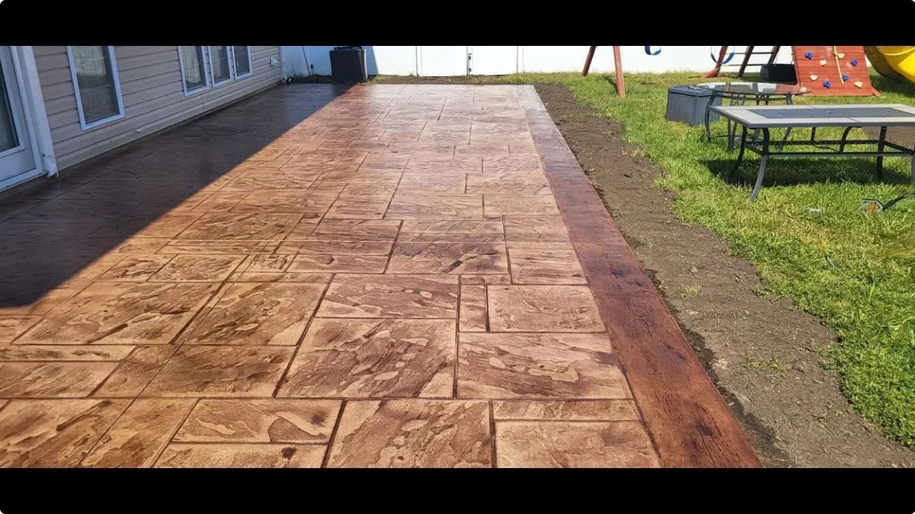 Stamped concrete patio with a border, next to a house and grass.