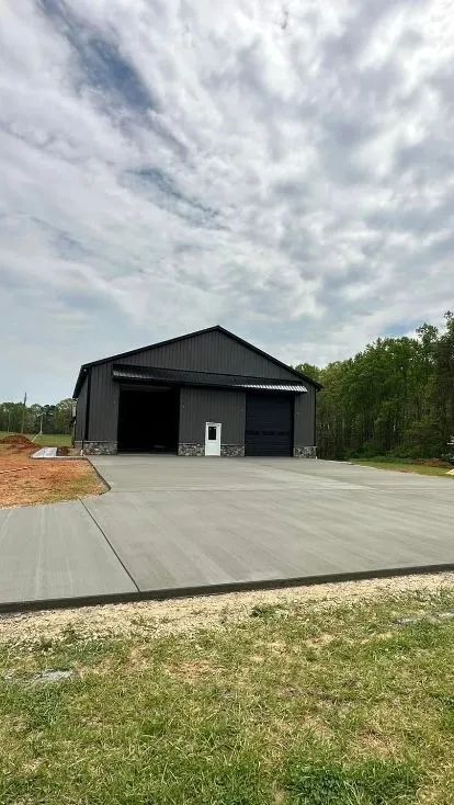 Gray metal building with large open doors, concrete apron, and a small white door.