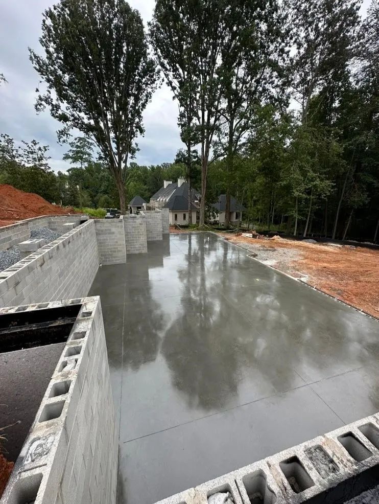 Concrete foundation with cinder block walls in front of a house under construction; trees in background.
